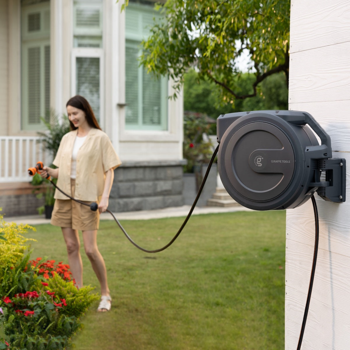 Woman using the hose connected to a wall-mounted  retractable hose reel in a garden setting.