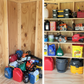 Before and after comparison showing bottles, cans and yard tools on the floor inside an unfinished shed versus the after showing all of the items neatly organized on the stud-mounted shed shelf bracket kit with boards for shelves.