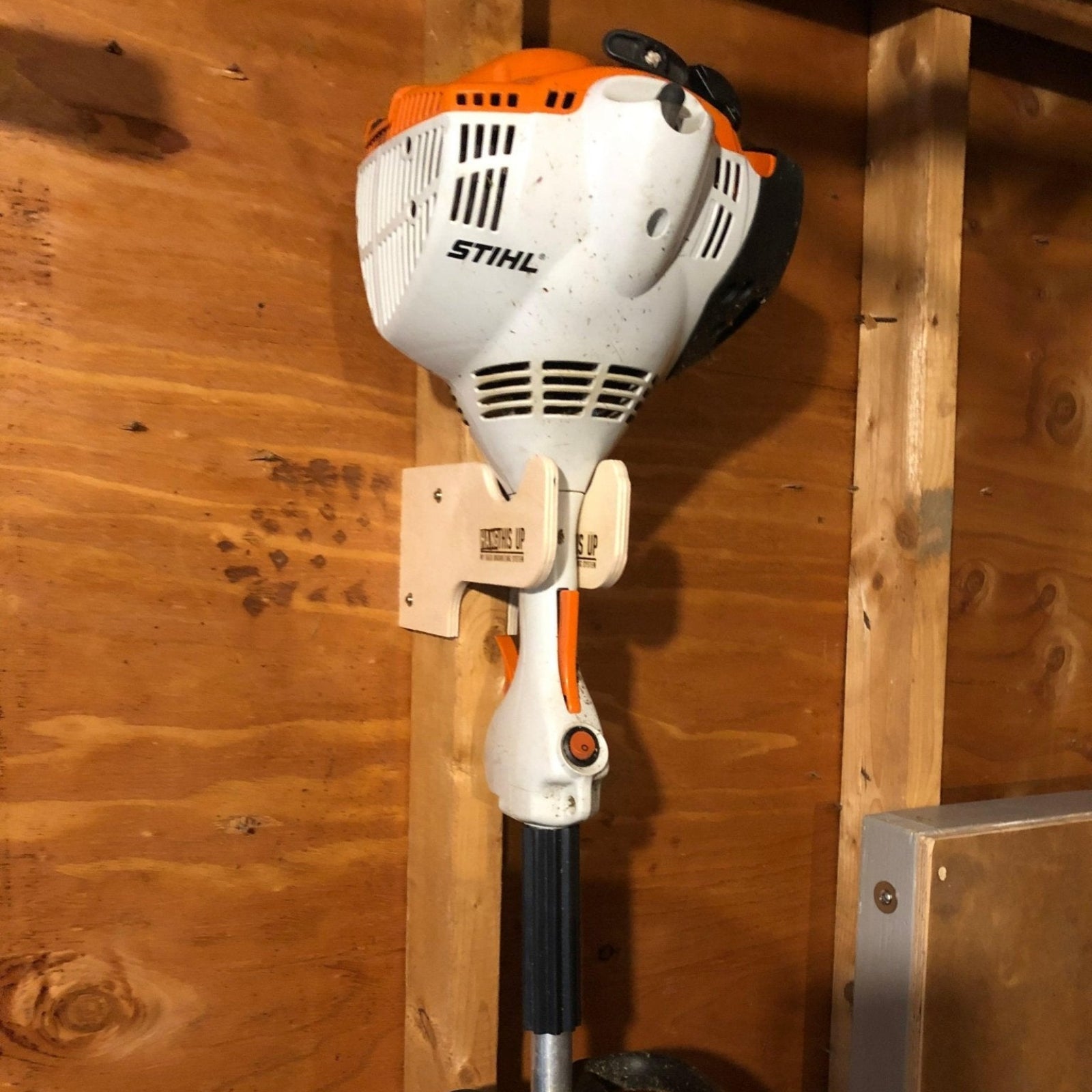 Weed whacker organizer installed on an unfinished shed wall with a weed whacker hanging neatly. 