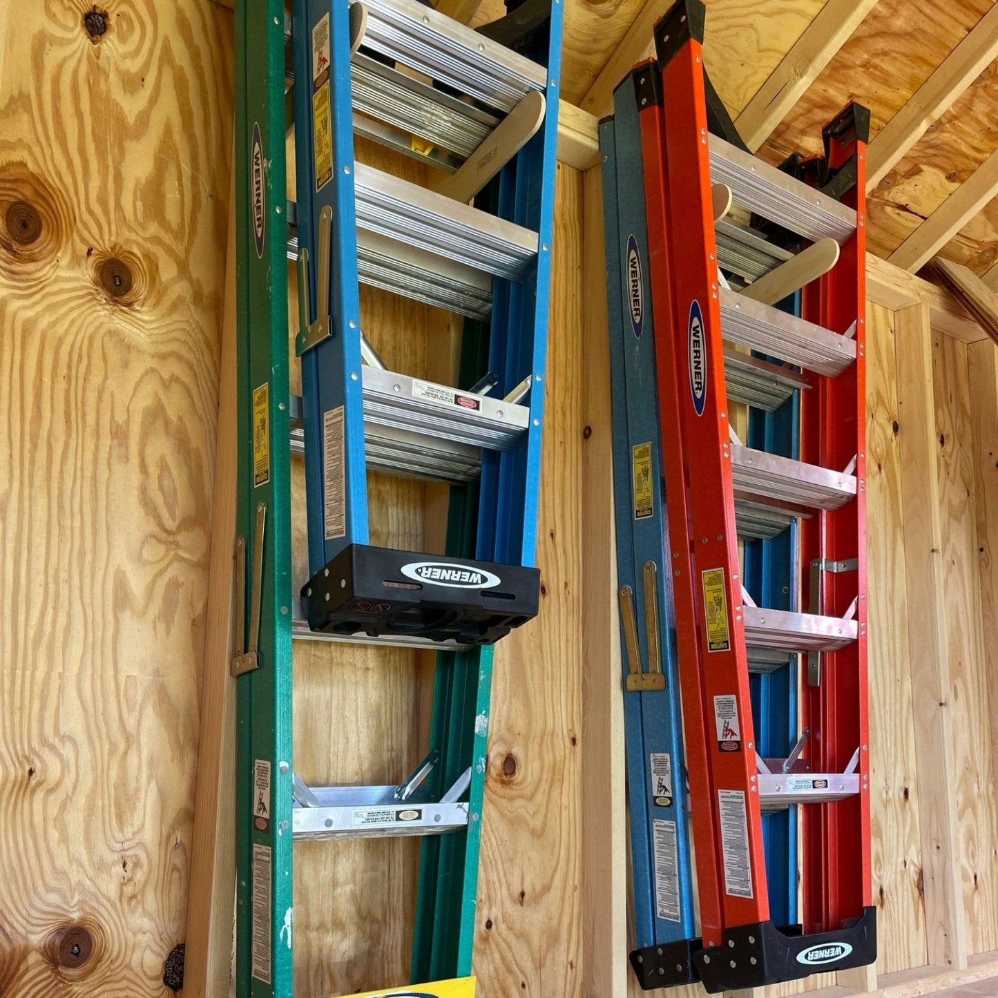 Two pairs of Step Ladder Organizers installed on an unfinished shed wall with step ladders hanging neatly.