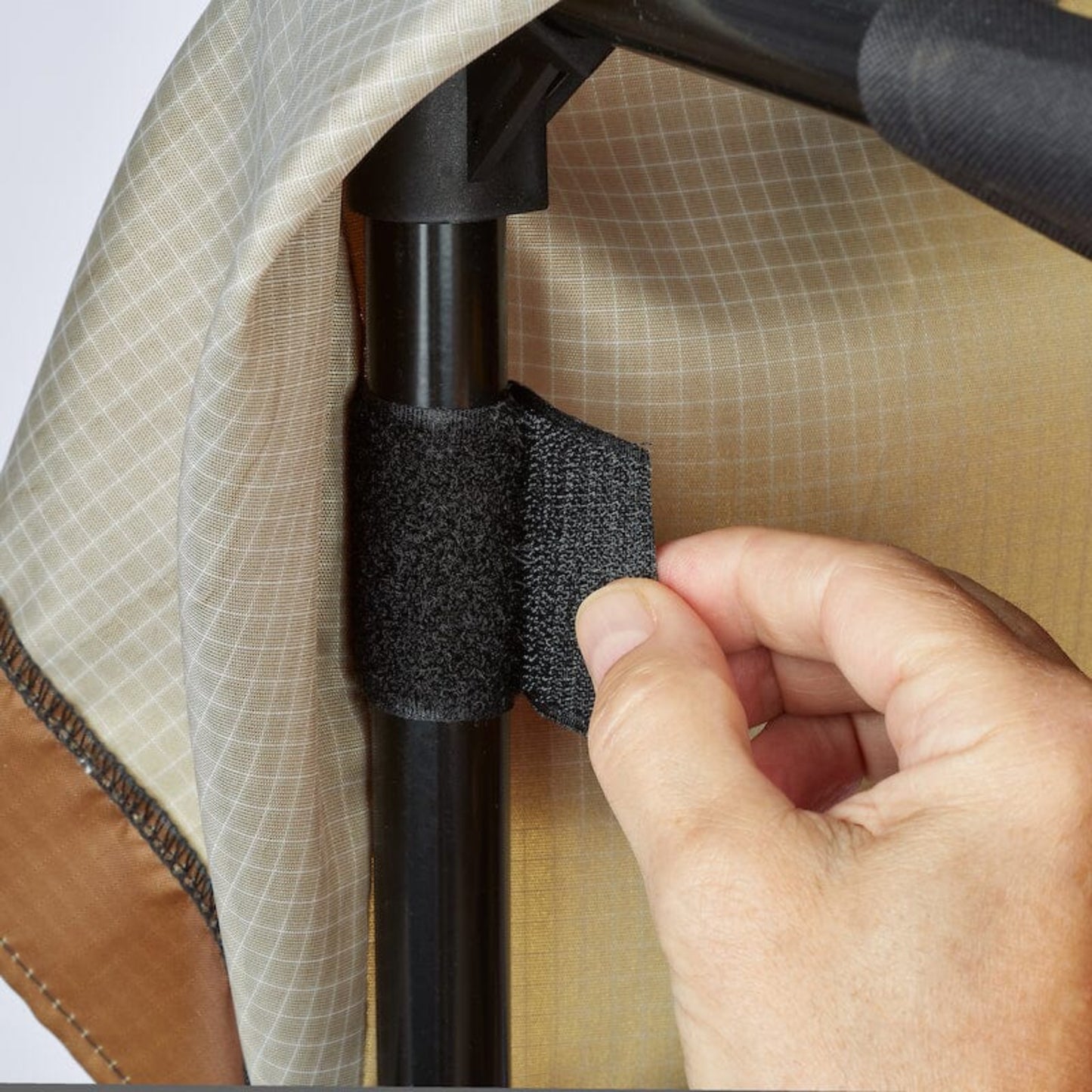 Hand adjusting a Velcro strap on a Urban Worm Bag Weather Cover on a white background. 