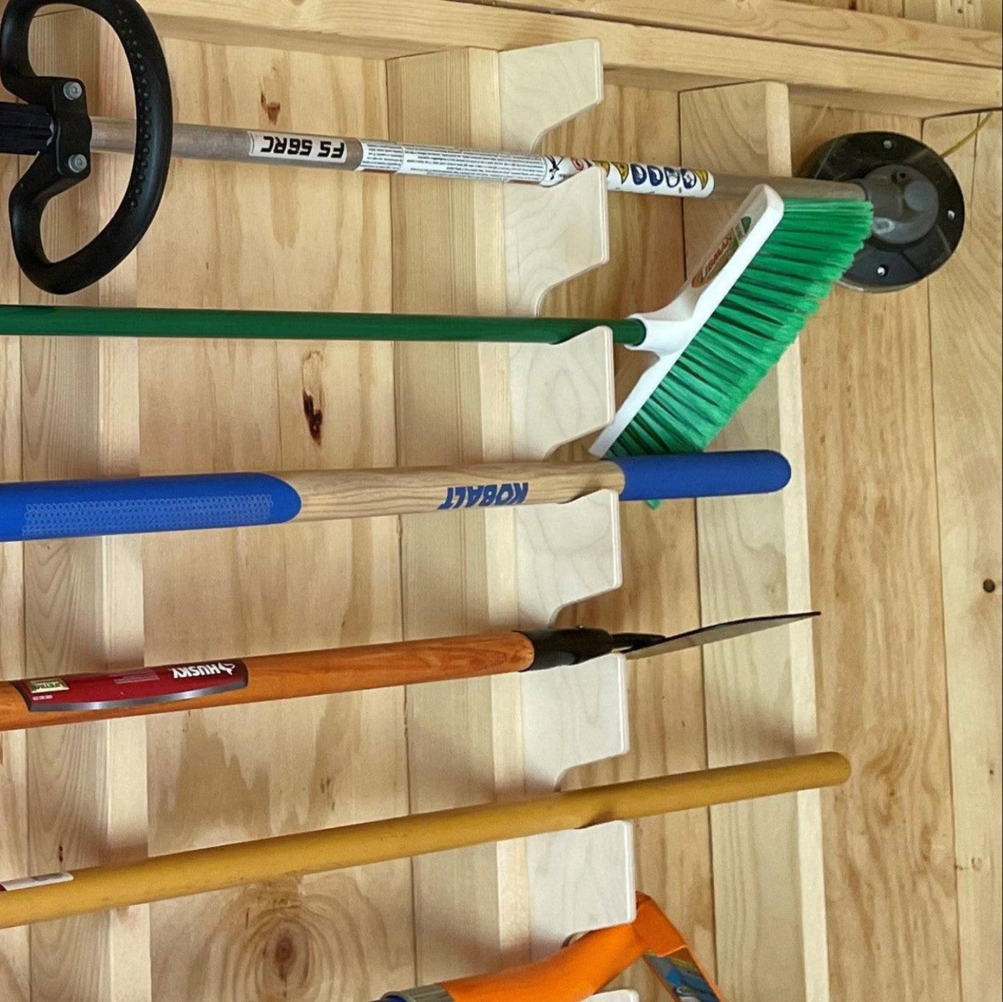 Close-up of a vertical garden tool organizer installed on the stud and garden tools in the rack.