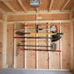 Stud-mounted vertical garden tool organizer rack holding multiple garden tools, neatly organized inside an unfinished shed.