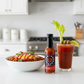 Big Red One Hot Sauce bottle on a white kitchen counter beside a bowl of chili and a glass of Blood Mary drizzled with spicy hot sauce.