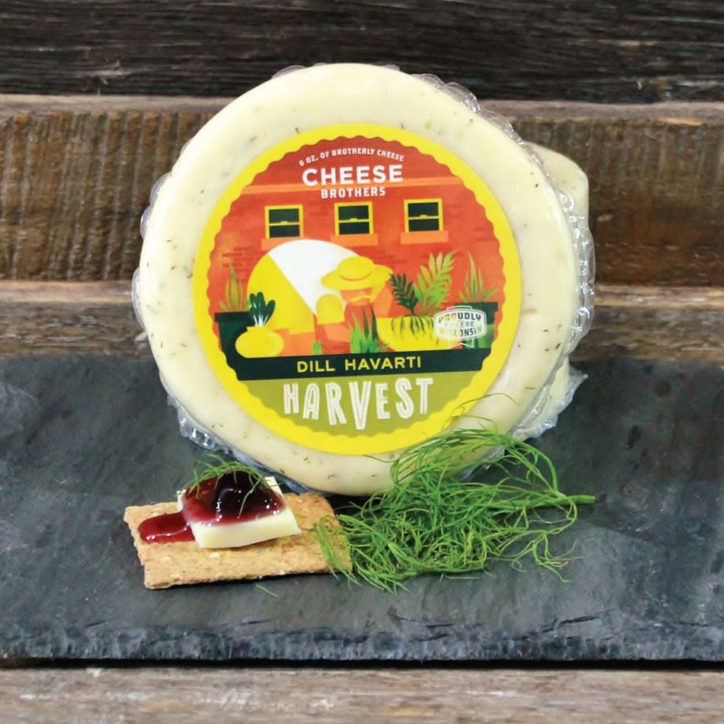 Block of Dill Havarti cheese presented on a serving platter with decorative elements such as herbs and the cheese spread on a cracker topped with jam