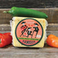Three amigos gouda cheese block presented on a wooden surface surrounded by three peppers, jalapeno, habanero, and chipotle