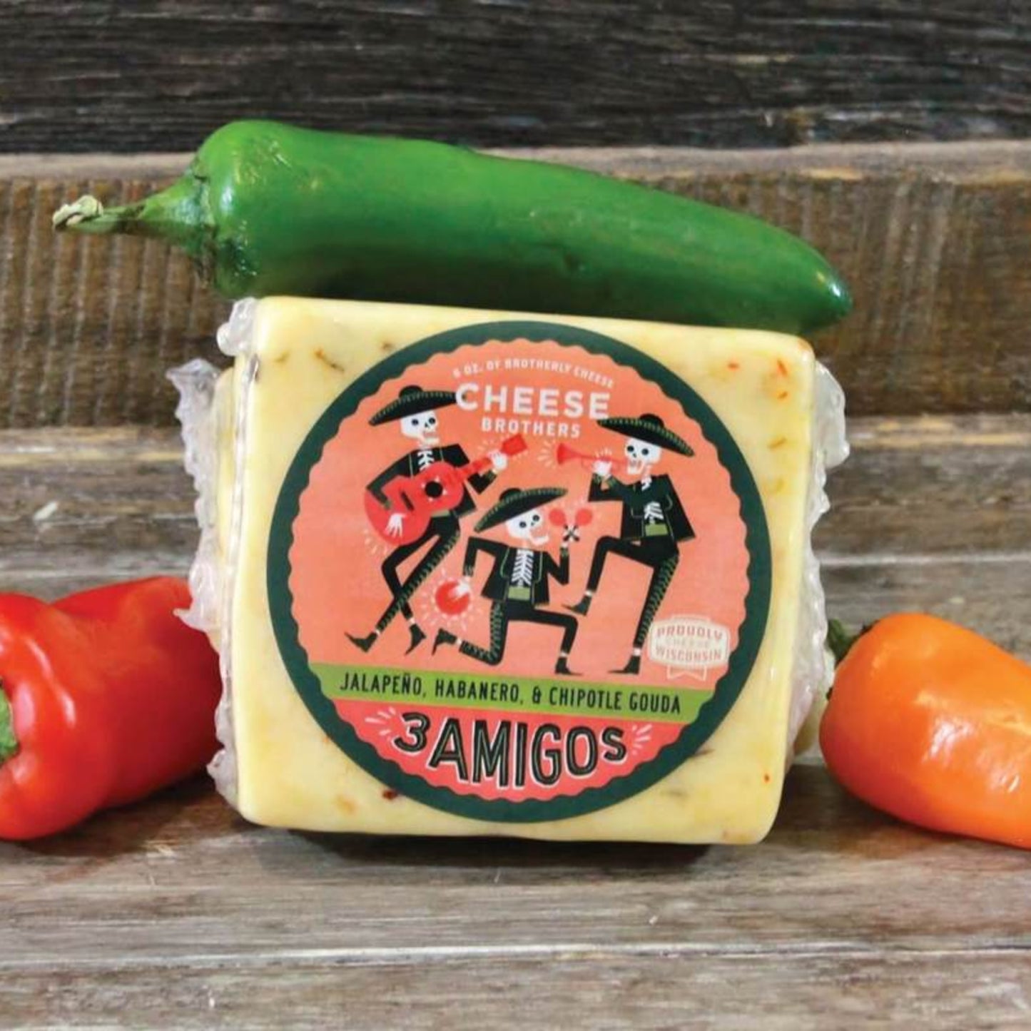 Three amigos gouda cheese block presented on a wooden surface surrounded by three peppers, jalapeno, habanero, and chipotle