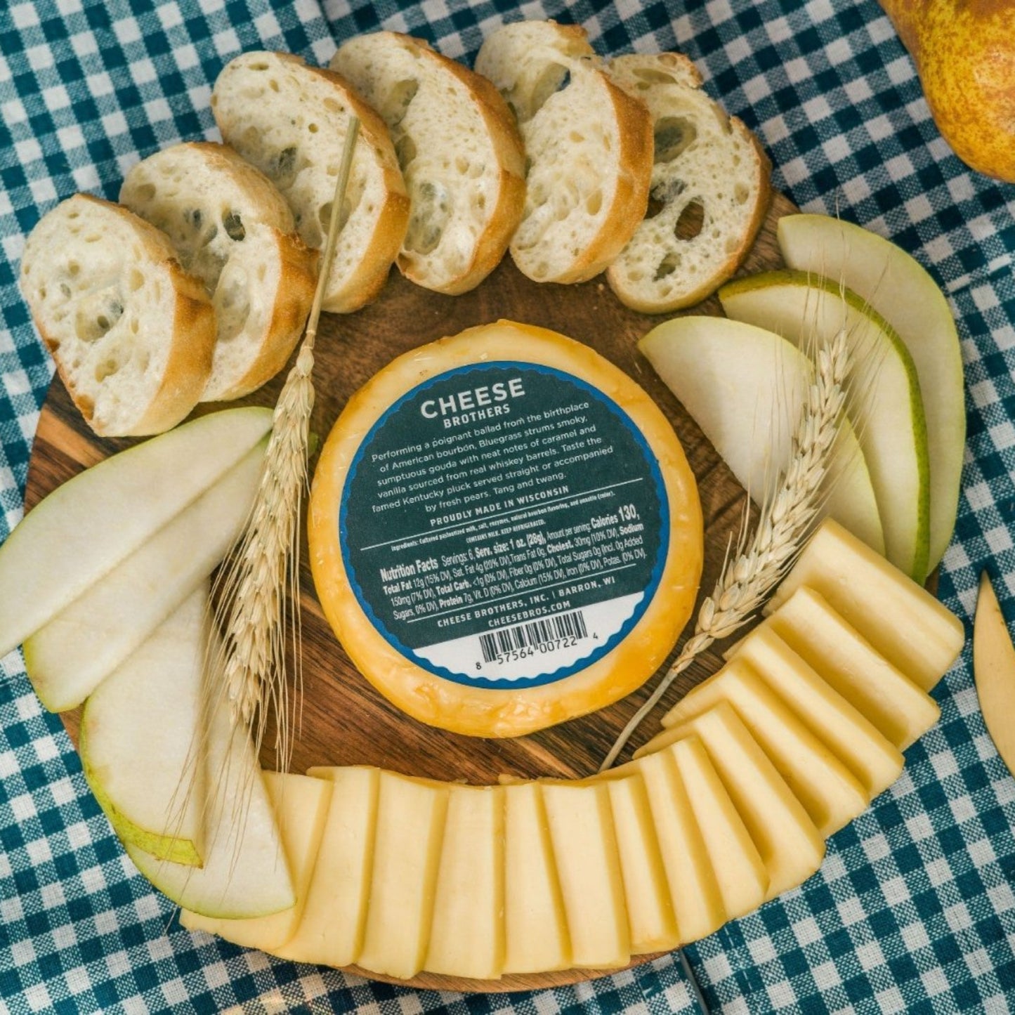 Bourbon Gouda block of cheese presented on a serving tray showing nutrition label with decorative elements such as sliced pears, sliced cheese, and wheat on a blue and white checkered tablecloth
