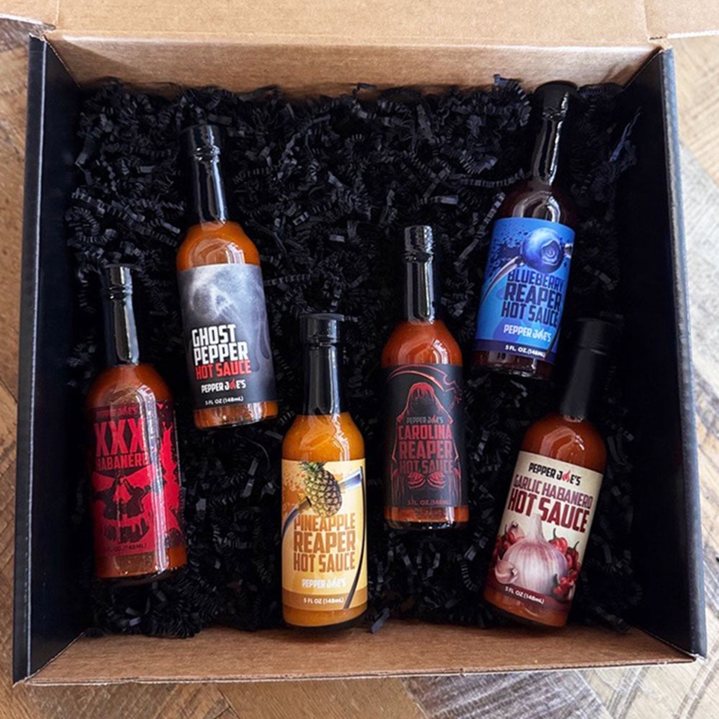 Pepper Joe’s Build Your Own 6-Pack hot sauce gift box featuring six assorted flavors, including XXX Habanero, Ghost Pepper, Pineapple Reaper, Carolina Reaper, Blueberry Reaper, and Garlic Habanero sauces, displayed in black crinkle packaging.