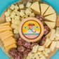 Wooden cheese board with various types of cheese and sausages on a blue background.