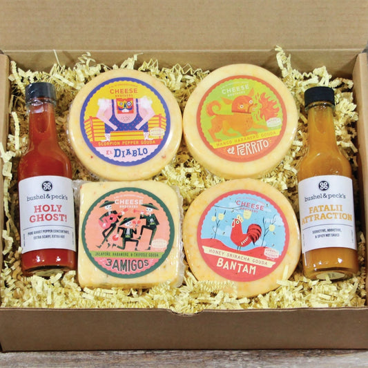 An open gift box displaying four blocks of cheese with different flavors, and two bottles of hot sauce.
