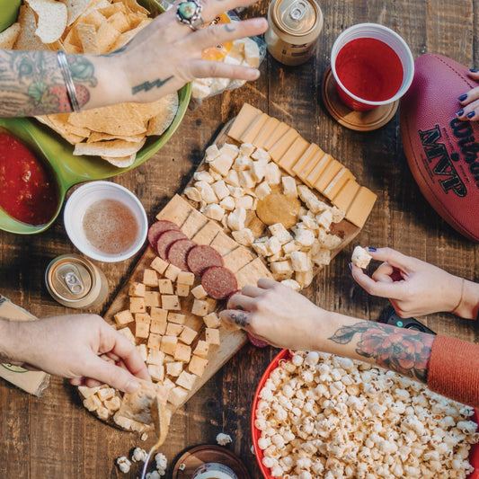 game day cheese giftbox lifestyle photo shoot with people gathered around charcuterie and other game day snacks