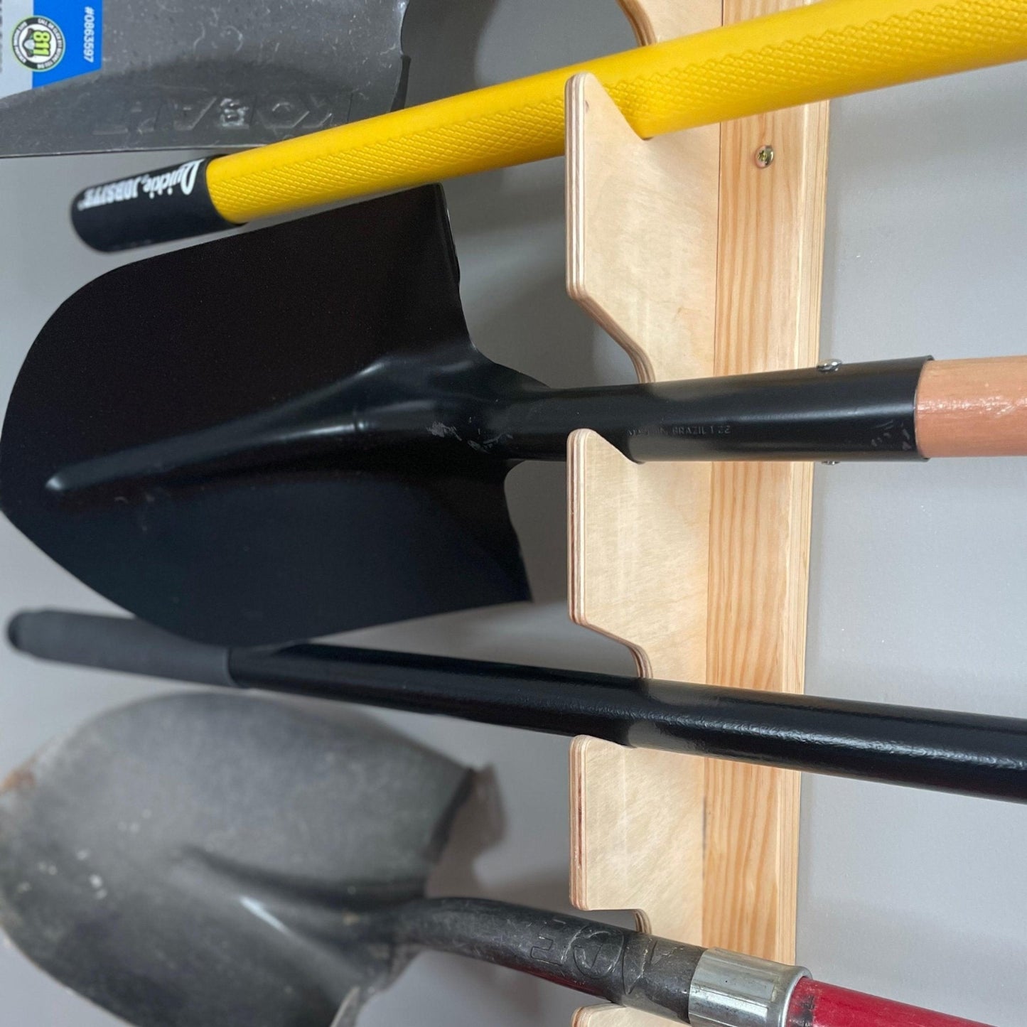 Close-up of flush-mounted garden tool rack holding shovels and yard tools, showing the slotted wooden design securely supporting tool handles.