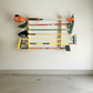 Flush-mounted garden tool rack holding a variety of yard tools including a trimmer, shovel, broom, rake, and hoe, shown installed in a clean garage.