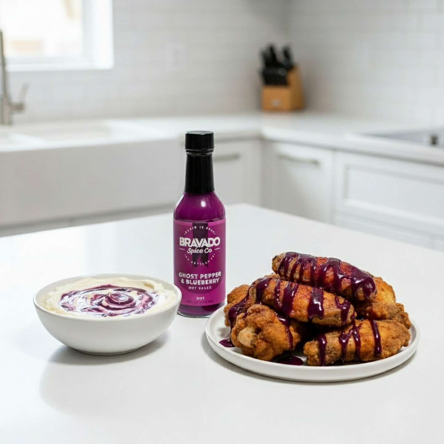 Ghost Pepper & Blueberry Hot Sauce bottle on a white kitchen counter beside a bowl of cream cheese dip and a plate of fried chicken wings drizzled with spicy blueberry hot sauce.