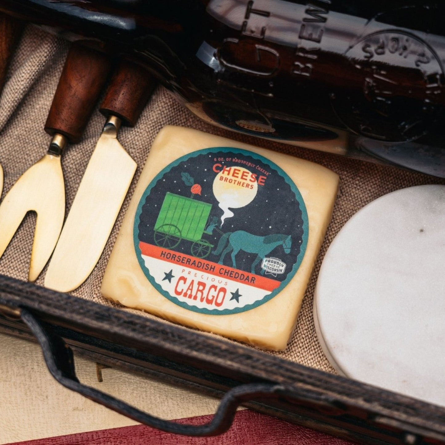 Horseradish Cheddar block displayed with cheese spreader, cheese knife, and bottle of wine