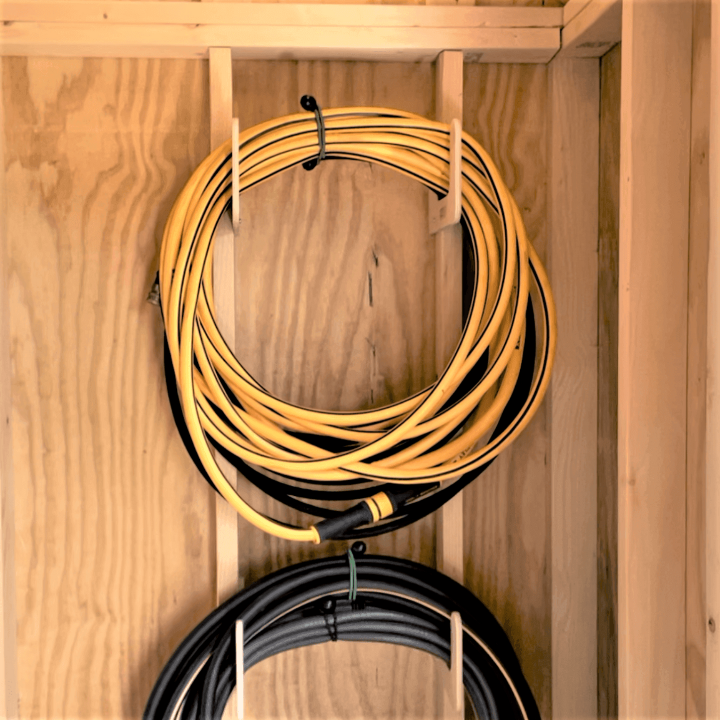Close-up of two hose organizers installed on studs and each organizer holding one hose. 