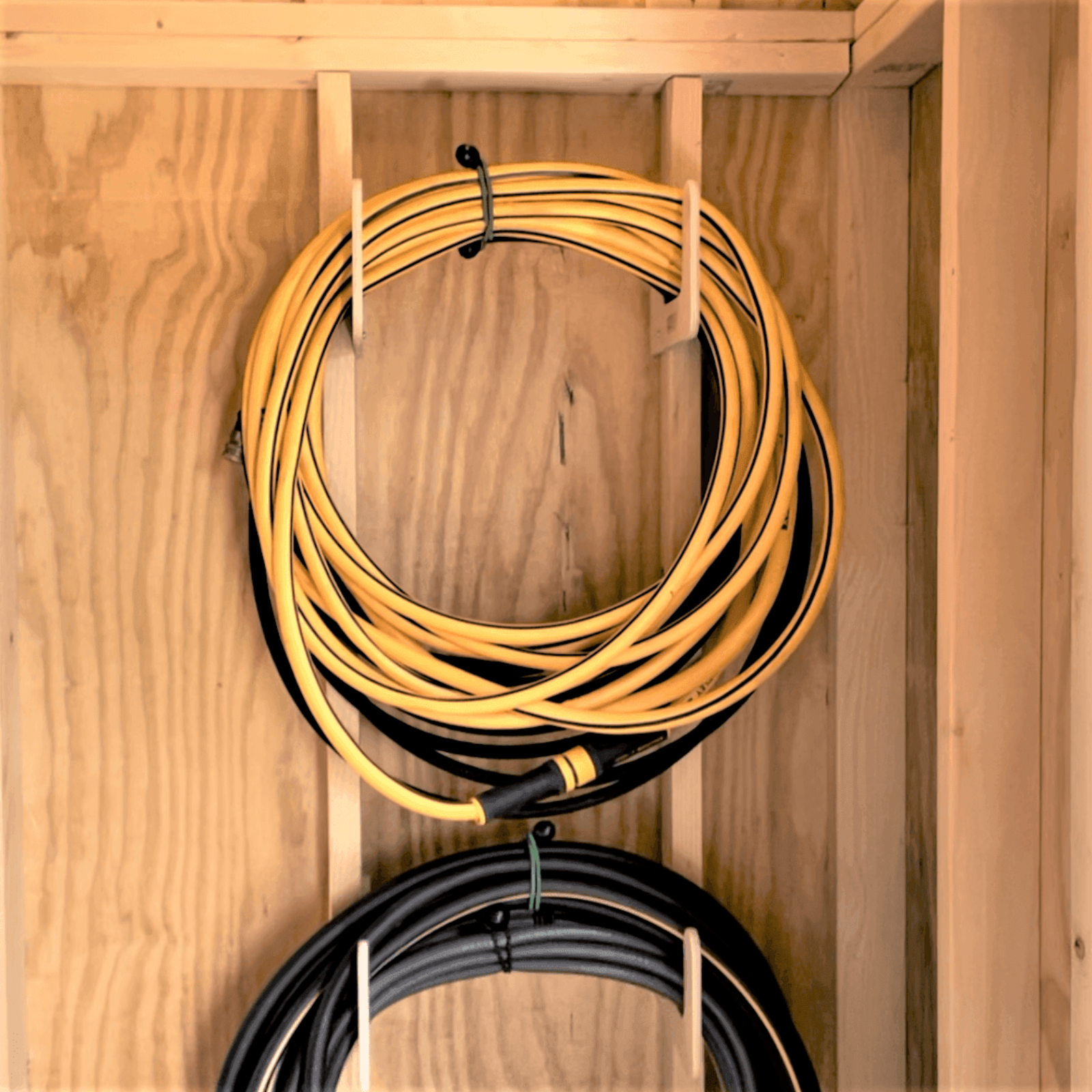 Close-up of two hose organizers installed on studs and each organizer holding one hose. 