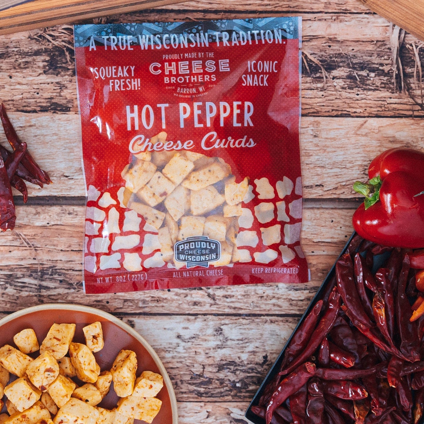 Hot pepper cheese curds package next to dried and fresh peppers and cheese curds in a bowl on a wooden surface