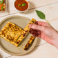 person holding sliced jalapeno golden baked bliss cheese over tan plate on white wooden table