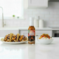 Mango Habanero Hot Sauce bottle on a white kitchen counter beside a rice bowl with vegetables and a plate of tacos drizzled with spicy hot sauce.
