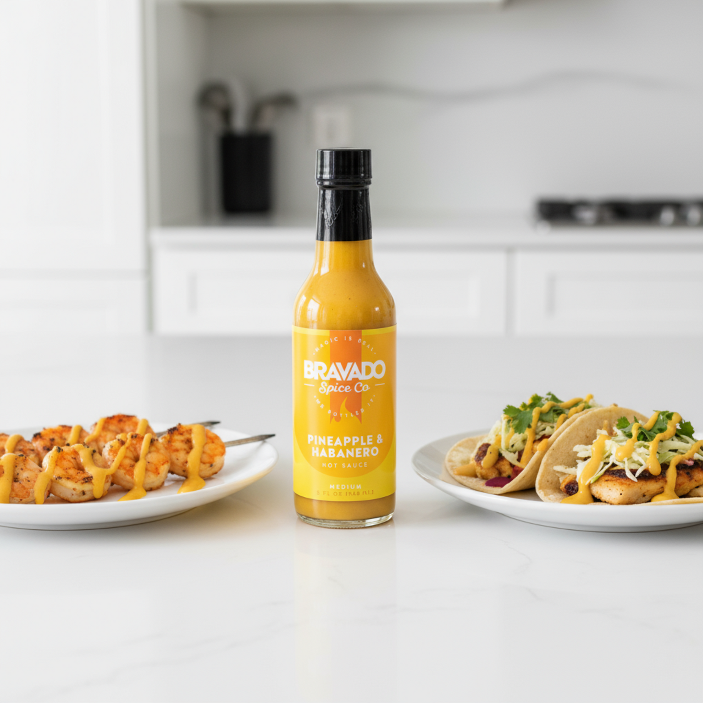Pineapple & Habanero Hot Sauce bottle on a white kitchen counter beside a plate of grilled shrimp and a plate of tacos drizzled with hot sauce.