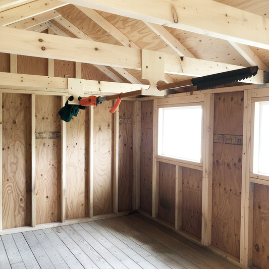 Stud-mounted pole saw and pool equipment organization rack holding a pole saw, inside an unfinished shed wall.