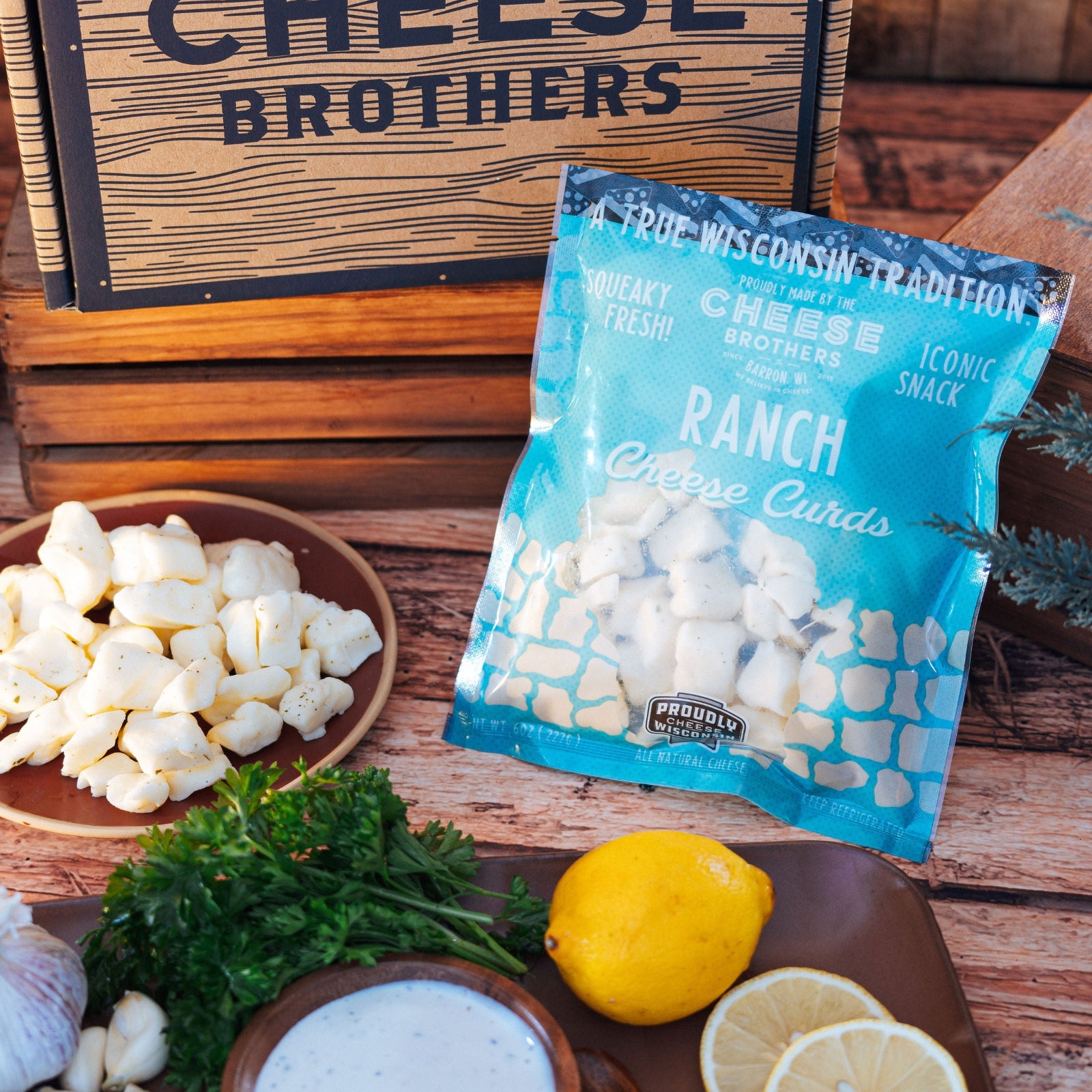 Bag of ranch cheese curds on a wooden surface with herbs, bowl of curds, and lemons