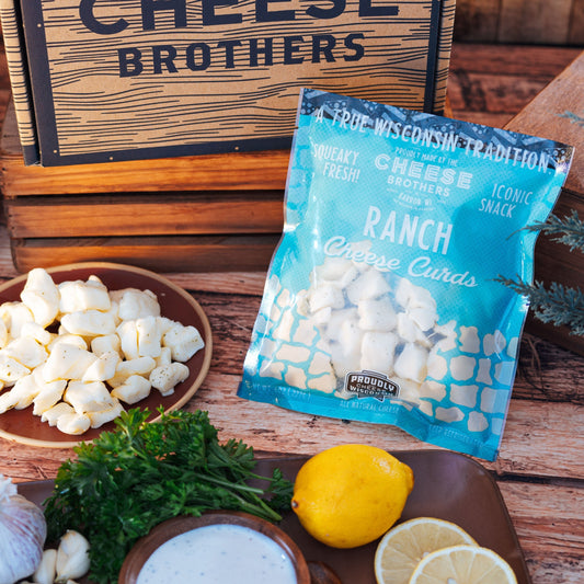 Bag of ranch cheese curds on a wooden surface with herbs, bowl of curds, and lemons