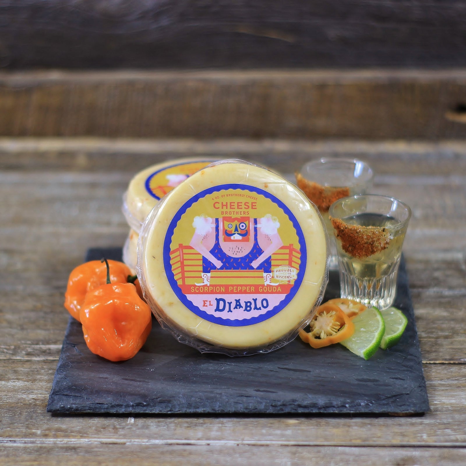 Scorpion pepper gouda cheese wheel next to hot peppers on slate cutting board