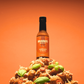 Serrano & Basil hot sauce bottle on a pile of fried chicken with basil leaves against an orange background