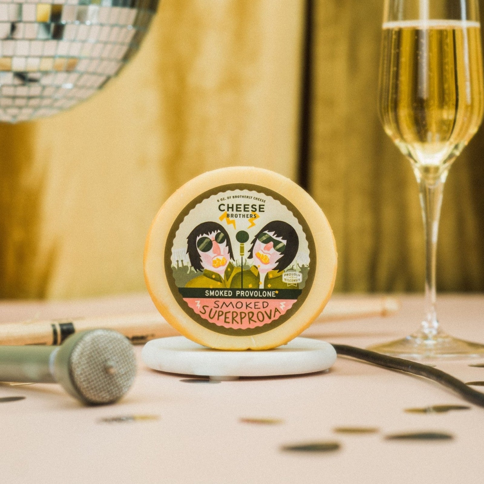 A  provolone cheese wheel is displayed on a table with a microphone, disco ball, and a glass of champagne in the background 