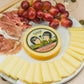 Smoked Provolone cheese wheel presented on serving platter with sliced cheese, deli meat, and grapes.
