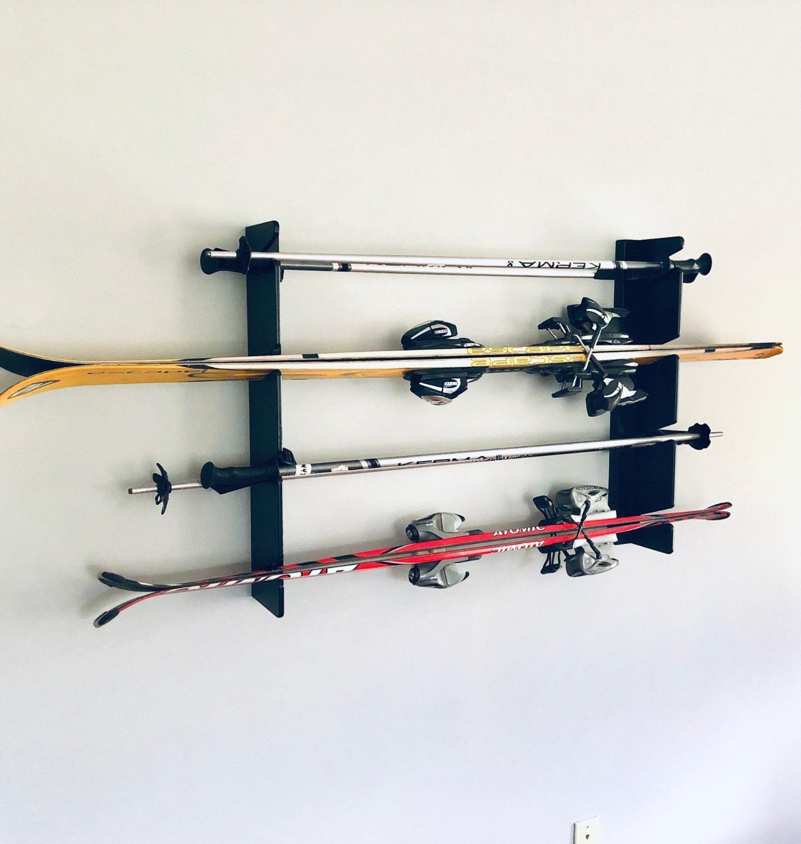 Flush-mounted ski rack in black finish holding multiple pairs of snow skis and poles, neatly organized on a wall.