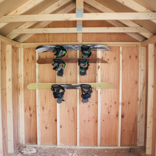 Stud-mounted snowboard organization rack holding multiple snowboards, neatly organized inside an unfinished shed wall.