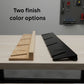 Two snowboard rack color finish options displayed on a workbench, showing natural wood and black versions side by side ion a garage workbench.