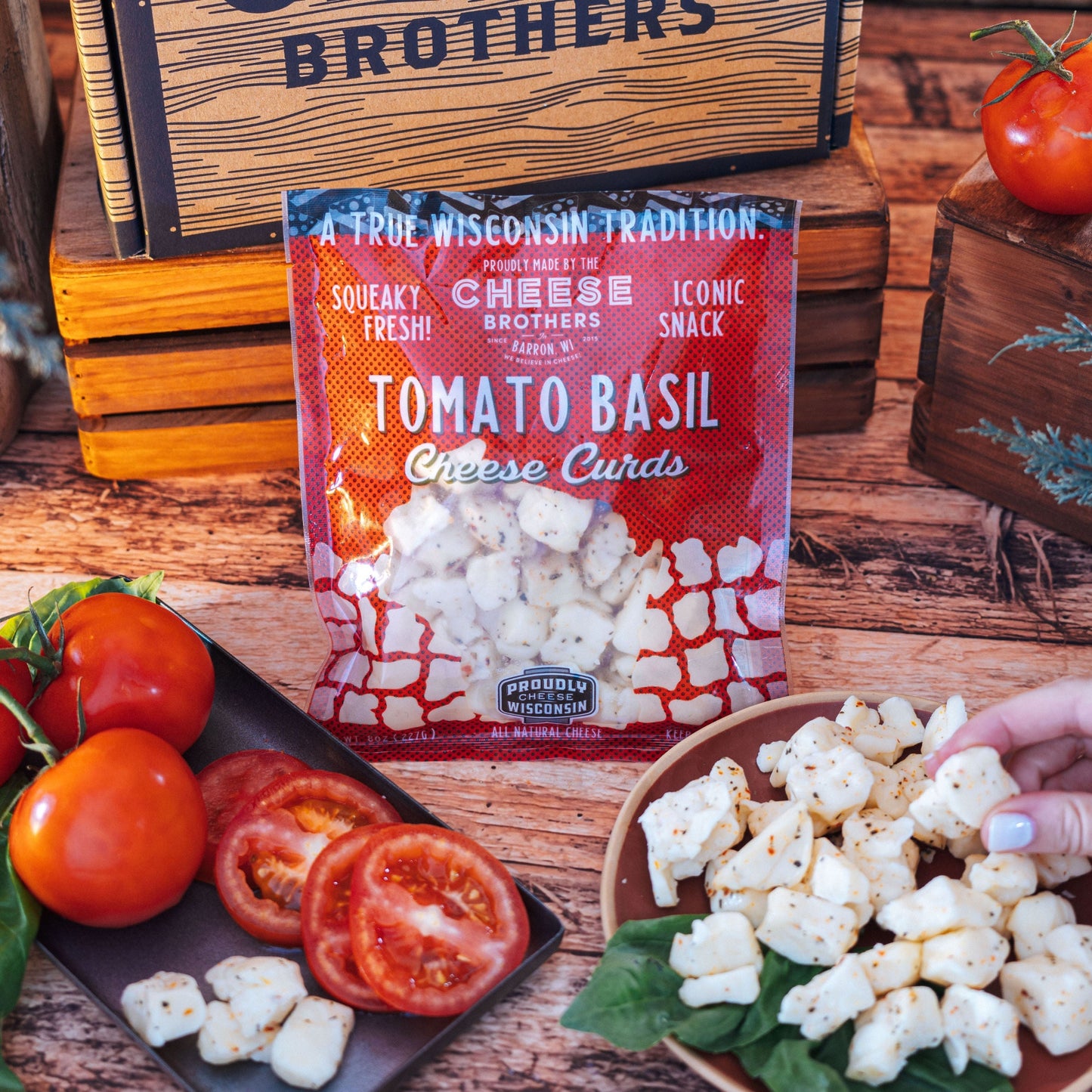 Package of Tomato Basil cheese curds with a visual representation of the cheese curds next to sliced tomatoes and basil leaves on a wooden surface.
