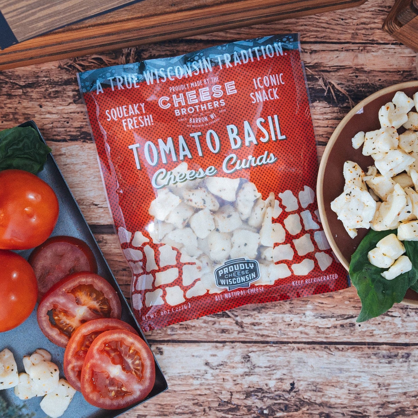 Package of Tomato Basil cheese curds with a visual representation of the cheese curds next to sliced tomatoes and basil leaves on a wooden surface.