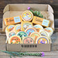An assortment of cheese blocks presented inside box, including various flavors like gouda, havarti, and cheddar, with decorative elements like herbs and flowers.