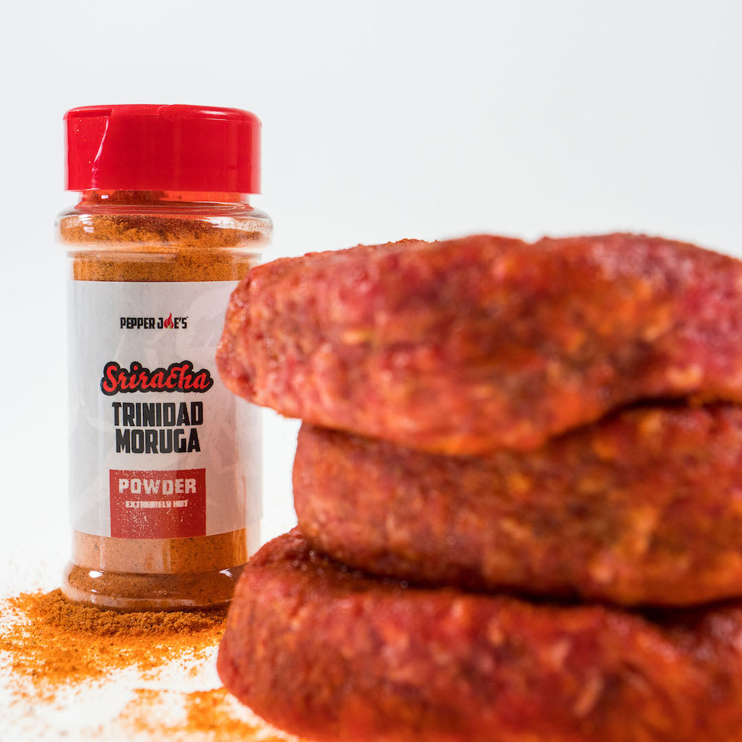 Pepper Joe's Sriracha Trinidad Scorpion Powder jar next to raw meat to use as seasoning and marinade